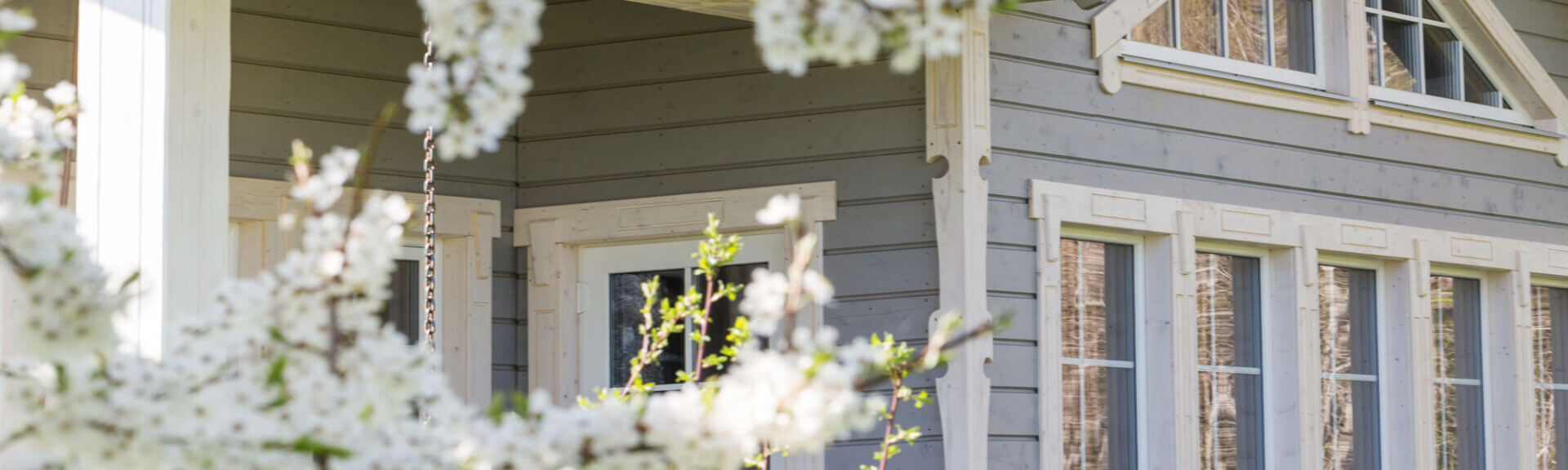 Beautiful Wooden House With Large Windows, A Showcase And A Terrace On The Background Of Blossoming Spring Trees